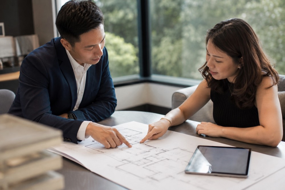 Consultant and buyer reading a floor plan together at a sales gallery table